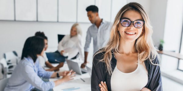 Employees Blonde female executive posing with smile and arms crossed during brainstorm with managers. Indoor portrait of european student spending time in hall with asian and african friends.